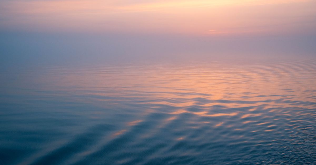 Peaceful ocean scene with calming ripples at sunset creating a gradient sky reflection.